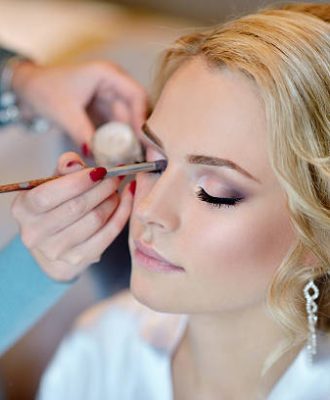 Wedding makeup artist making a make up for bride. Beautiful sexy model girl indoors. Beauty woman with curly hair. Female portrait. Bridal morning of a cute lady. Close-up hands near face